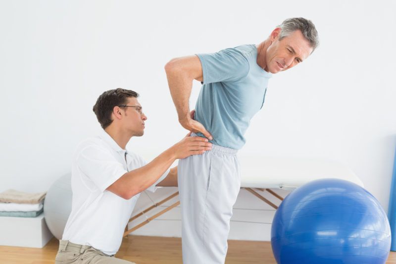 Side view of a male therapist massaging mans lower back in the gym at hospital