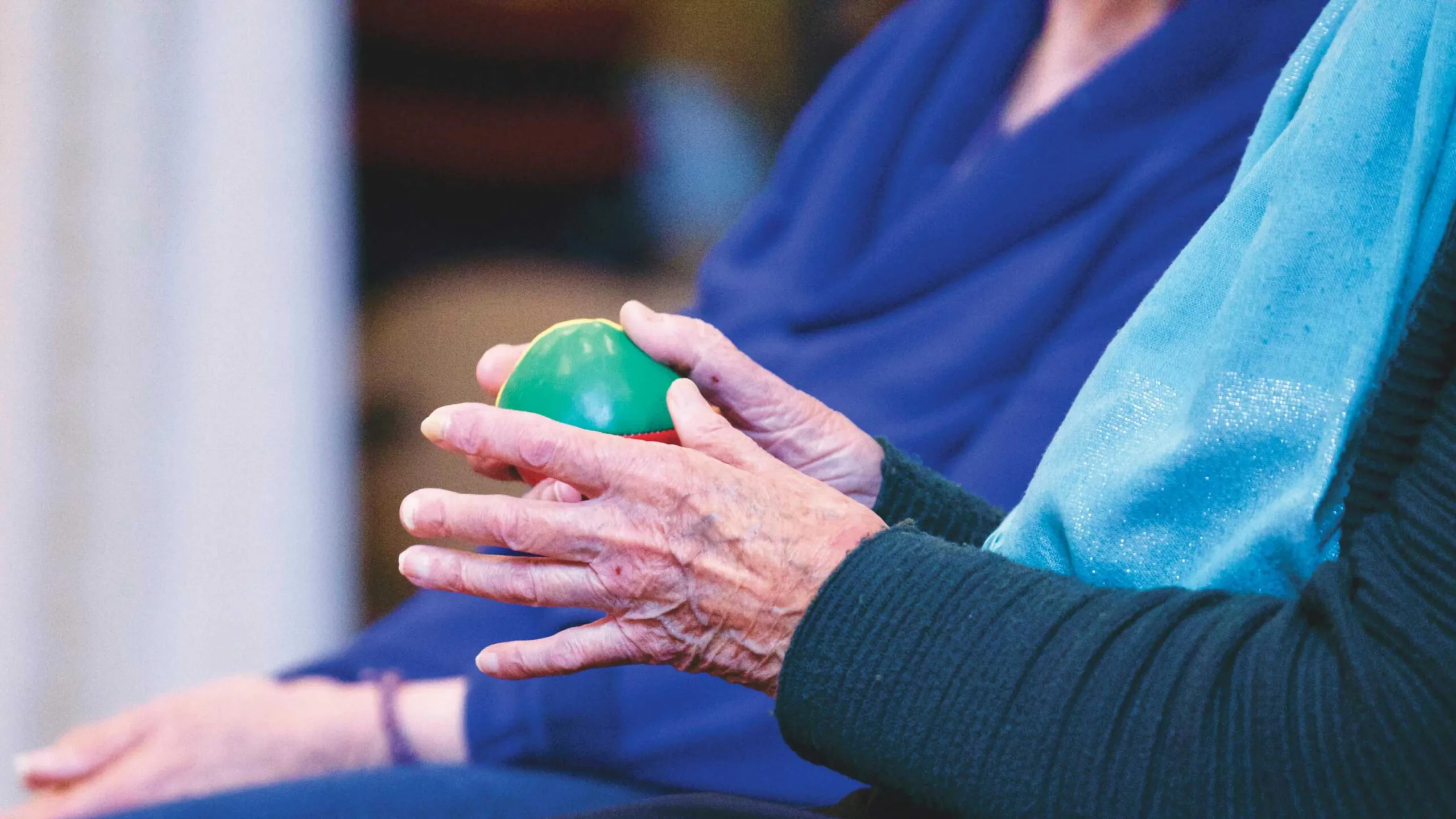 a pair of hands from an senior citizen holding a green ball for rehab purposes