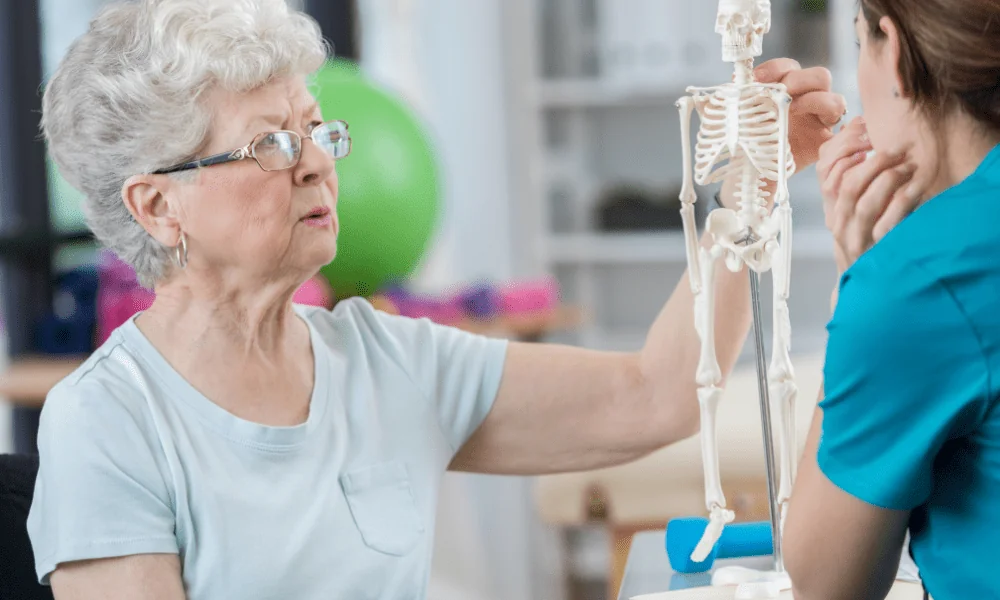 female patient discusses osteoporosis with her therapist while studying model skeleton