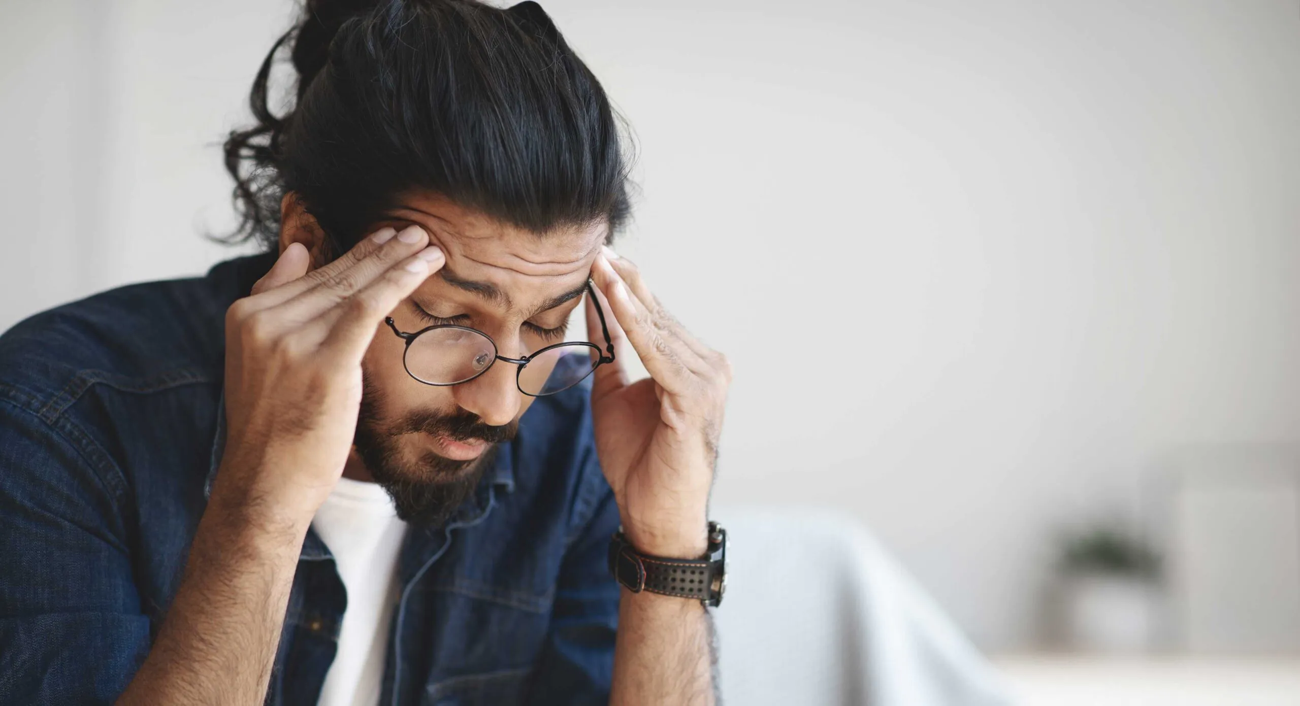a man in glasses holding his temples do to head pain